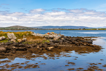 Bay with low tide, seaweeds, boat and mountains in Carraroe