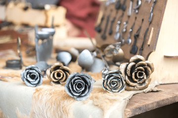 Five metal roses of multicolored metals on the table at the seasonal fair of masters.