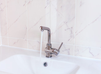 Faucet pouring water into white sink in domestic bathroom.