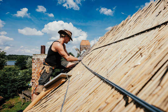 Man repairing thatch roof on sunny house