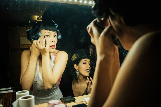 Female burlesque performers getting ready, applying makeup at dressing room mirror