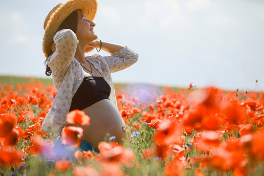Carefree pregnant woman in sunny, idyllic rural red poppy field