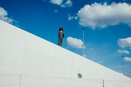 Cool, well-dressed young man with afro standing on sunny urban wall