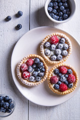 Cakes with raspberries and blueberries on a white plate sprinkled with icing sugar on a white wooden background Top view