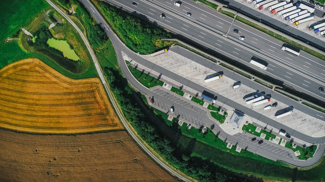 Drone Point Of View Semi-trucks Parked At Truck Stop Between Highway And Farmland, Bayern, Germany