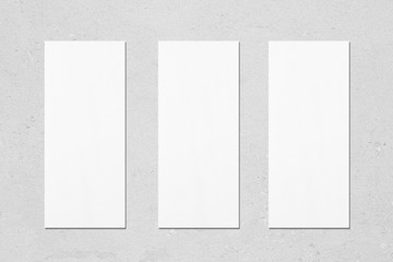 Three empty white vertical rectangle poster menu mockups with soft shadows on neutral light grey concrete wall background. Flat lay, top view - obrazy, fototapety, plakaty