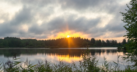 Orange-yellow sunrise through a strong cloud over the lake