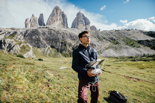 Boy with digital tablet and joystick controlling drone in sunny Drei Zinnen Nature Park, South Tyrol