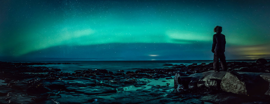 Teenage boy watching Northern Lights from rock, Reykjanesbaer, Iceland