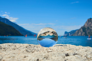 Lake Garda (Lago di Garda or Lago Benaco) seen through a glass crystal  ball placed on rock. Selective focus
