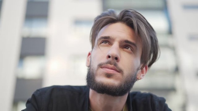 Closeup of handsome bearded man with pierced ear looking away dreamily, his hair waving in wind in slow motion