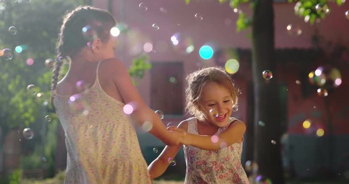 Authentic shot of two cute little girls sisters having fun to dance and playing with soap bubbles outside their house on a sunny day.