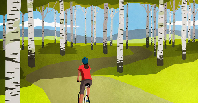 Woman mountain biking on path through trees in idyllic forest