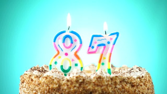 Birthday cake with a burning birthday candle. Number 87. Background changes color