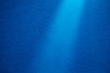 Light blue half-blurred vertical ray of light on a blue fine-textured background