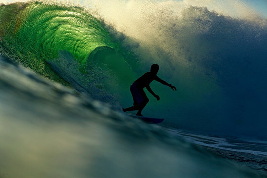 Silhouette male surfer riding backlit ocean wave