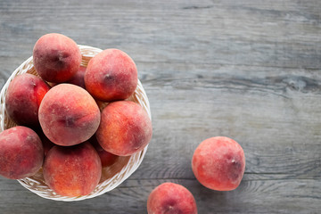 Ripe organic peaches in a white basket on a gray background.