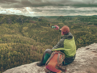 Backpacker with phone in hand. Spring valley in rocky mountains.