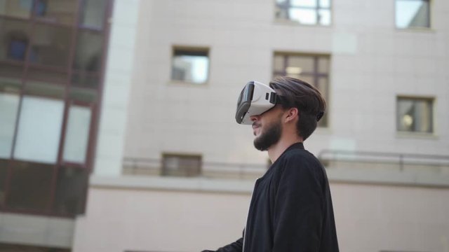 Panning slow motion shot of young man in vr headset standing in street and exploring data visualized in virtual reality. Man swiping and magnifying information