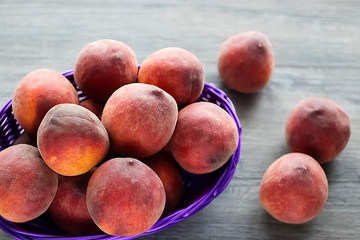 Ripe organic peaches in a purple basket on a gray background.