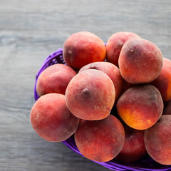 Ripe organic peaches in a purple basket on a gray background.