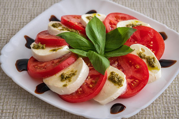 Plate of healthy classic delicious caprese salad with tomatoes and mozzarella cheese with fresh basil leaves on light linen tablecloth. Italian cuisine concept