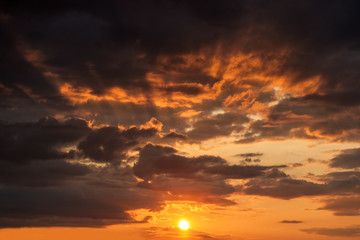 glow of sunset on a cloudy sky with the sun and rays behind the clouds
