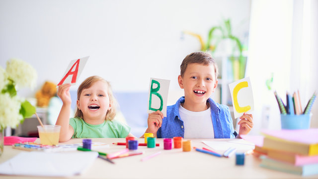 a little girl and a boy learn at home. happy kids at the table with school supplies smiling funny and learning the alphabet in a playful way.