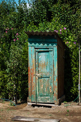 Fototapeta na wymiar Rustic outdoor toilet stands in the garden sparkling, reflecting the sunshine light