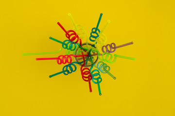 Spiral colorful straws on yellow background, flat lay