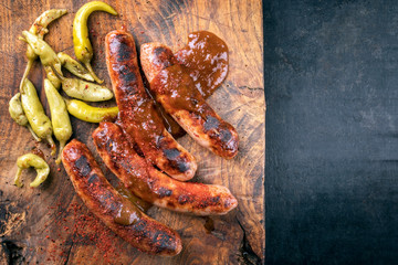 Traditional barbecue German Bratwurst with hot sauce and peperoni as top view on an old cutting board with copy space right