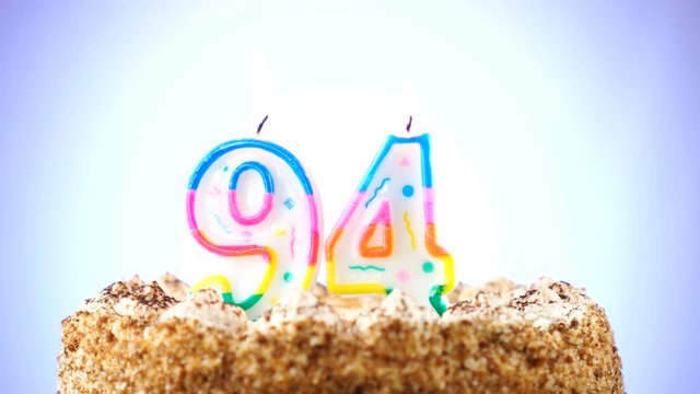 Birthday cake with a burning birthday candle. Number 94. Background changes color