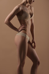 Thin young woman in underwear on beige background