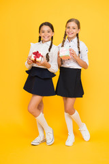 Gift shop. Happy small children holding gifts on yellow background. Little girls smiling with gift boxes. Adorable kids with beautifully wrapped birthday or school gift packs