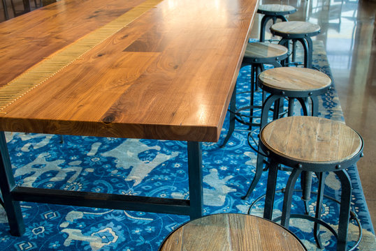a shiny wooden table with a row of  empty round rustic wooden stools on a blue carpet with copy space