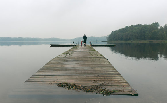 Father and a toddler daughter walking along boardwalk on a lake, Skane County, Sweden
