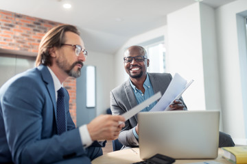 Dark-skinned businessman smiling while cooperating with colleague