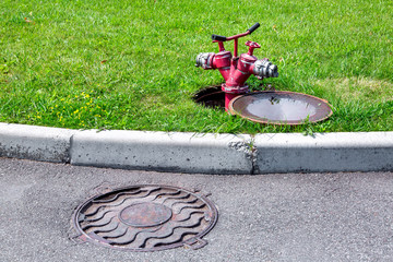 fire hydrant red pipe with a gate connected to an open hatch on a green lawn by an asphalt road...