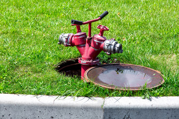 fire hydrant connected to an open manhole on a green lawn with grass, closeup of an open manhole...