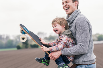 Father and son having fun, playing with skateboard outdoors