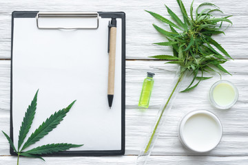 Cannabis cosmetic cream in a jar and a blank paper page with researching result and a green plant...