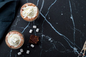 hot chocolate with cream in transparent mugs on black marble table. Copy space, top view