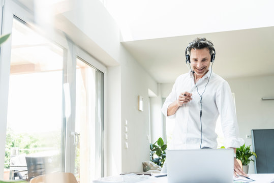 Businessman in bright office having conference call, using headset and laptop