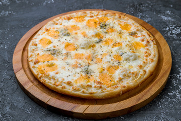 Pizza Quattro formaggi on wooden board on black concrete