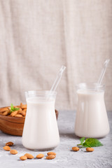 Organic non dairy almond milk in glass and wooden plate with almond nuts on a gray concrete background.