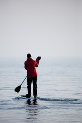 Guy in a red coat on a paddle surfboard in Lake Ontario
