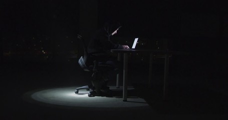 Hacker using laptop computer while working in dark office with big city light - Powered by Adobe