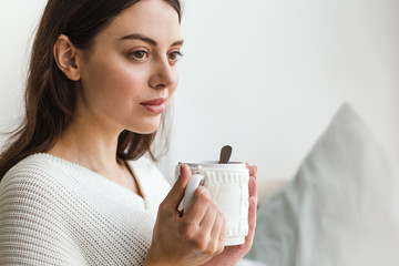 Beautiful face of a girl, a girl in white sweater sits on a sofa with a cup of hot tea in her hands