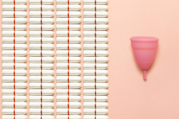 Reusable silicone menstrual cup and heap of tampons comparison on a soft pink background. Modern female intimate alternative gynecological hygiene. Eco zero waste concept