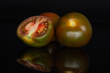 Group of two whole one half of round fresh greenish red tomato isolated on black glass